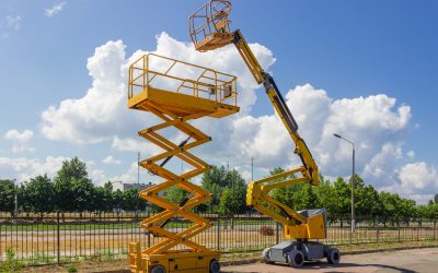 Yellow self propelled articulated boom lift and scissor lift on background of street with trees and sky